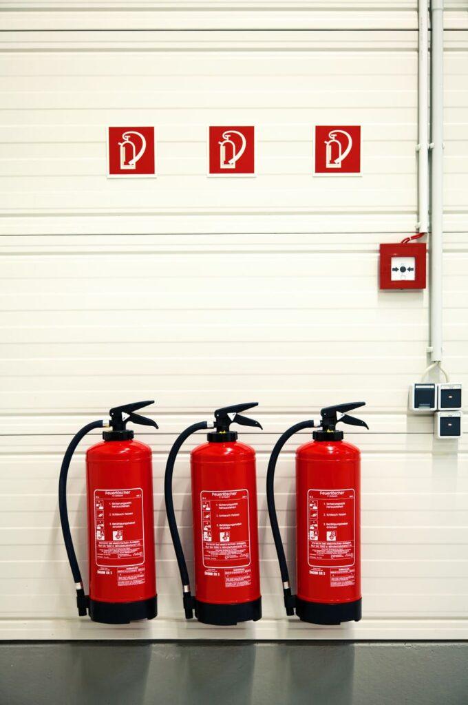 Drei Feuerlöscher unter Brandschutzzeichen in einer Industrieanlage, die klare Hinweise auf den Standort der Notausrüstung geben.