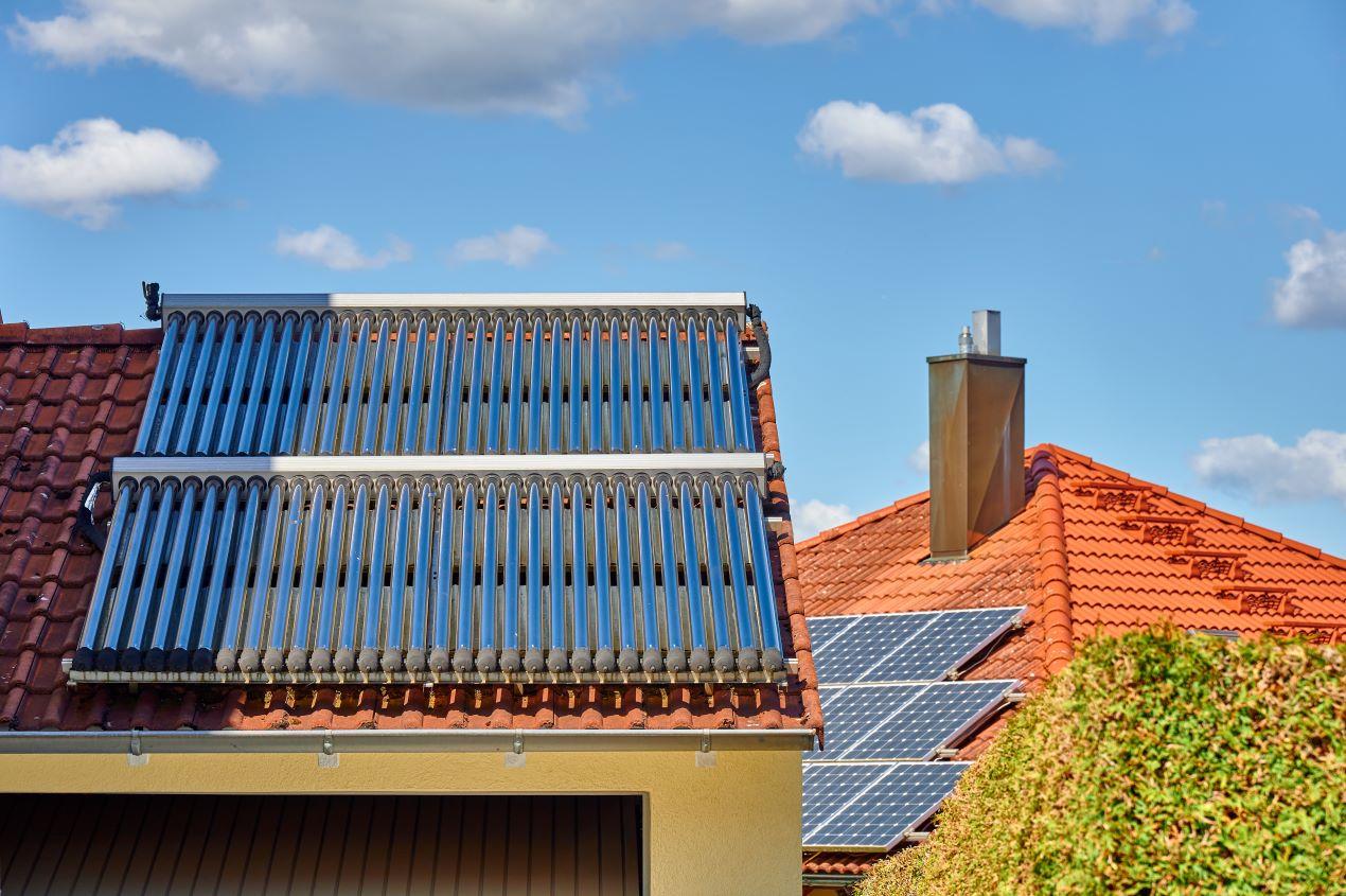 Solarthermie- und Photovoltaikanlagen auf roten Ziegeldächern eines Wohnhauses, nachhaltige Energiegewinnung. Ergänzende Heizlösungen zu wärmepumpe kaufen leipzig.