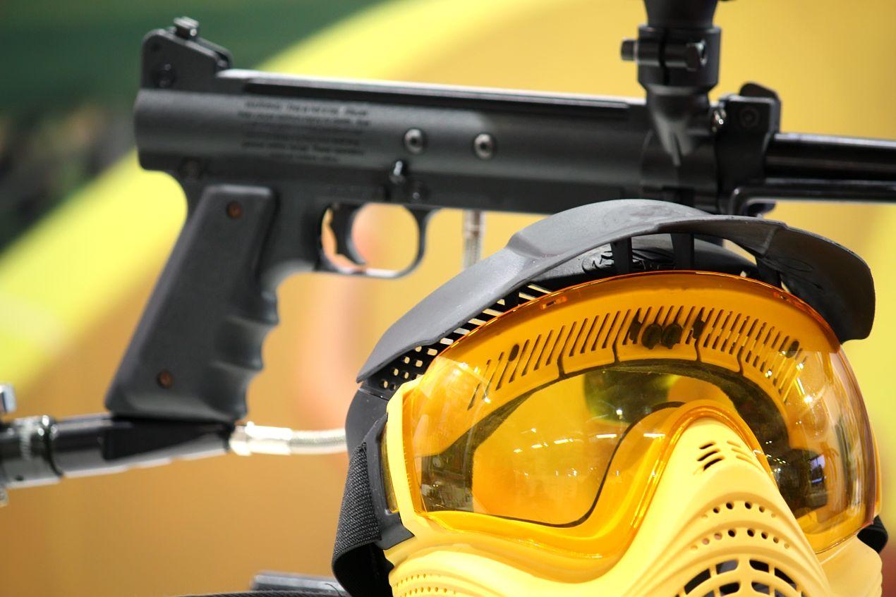 Nahaufnahme von Paintball Waffen mit gelber Schutzmaske auf Halterung, vor gelbem Hintergrund fotografiert