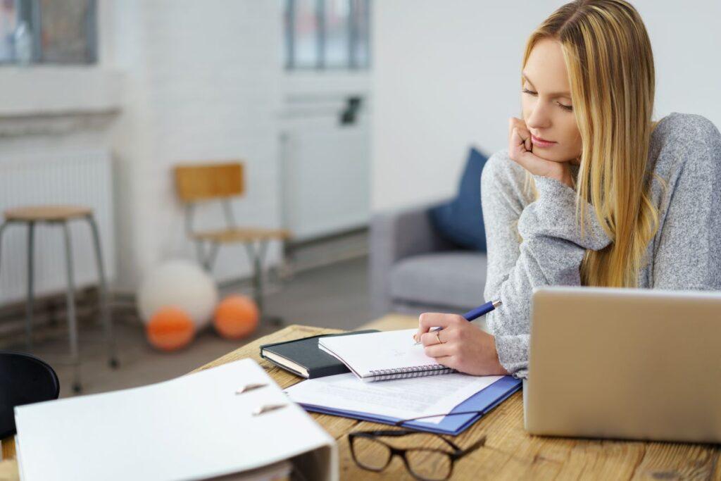 Nachdenkliche Studentin mit Notizen am Laptop bereitet sich intensiv auf das Masterarbeit schreiben lassen vor
