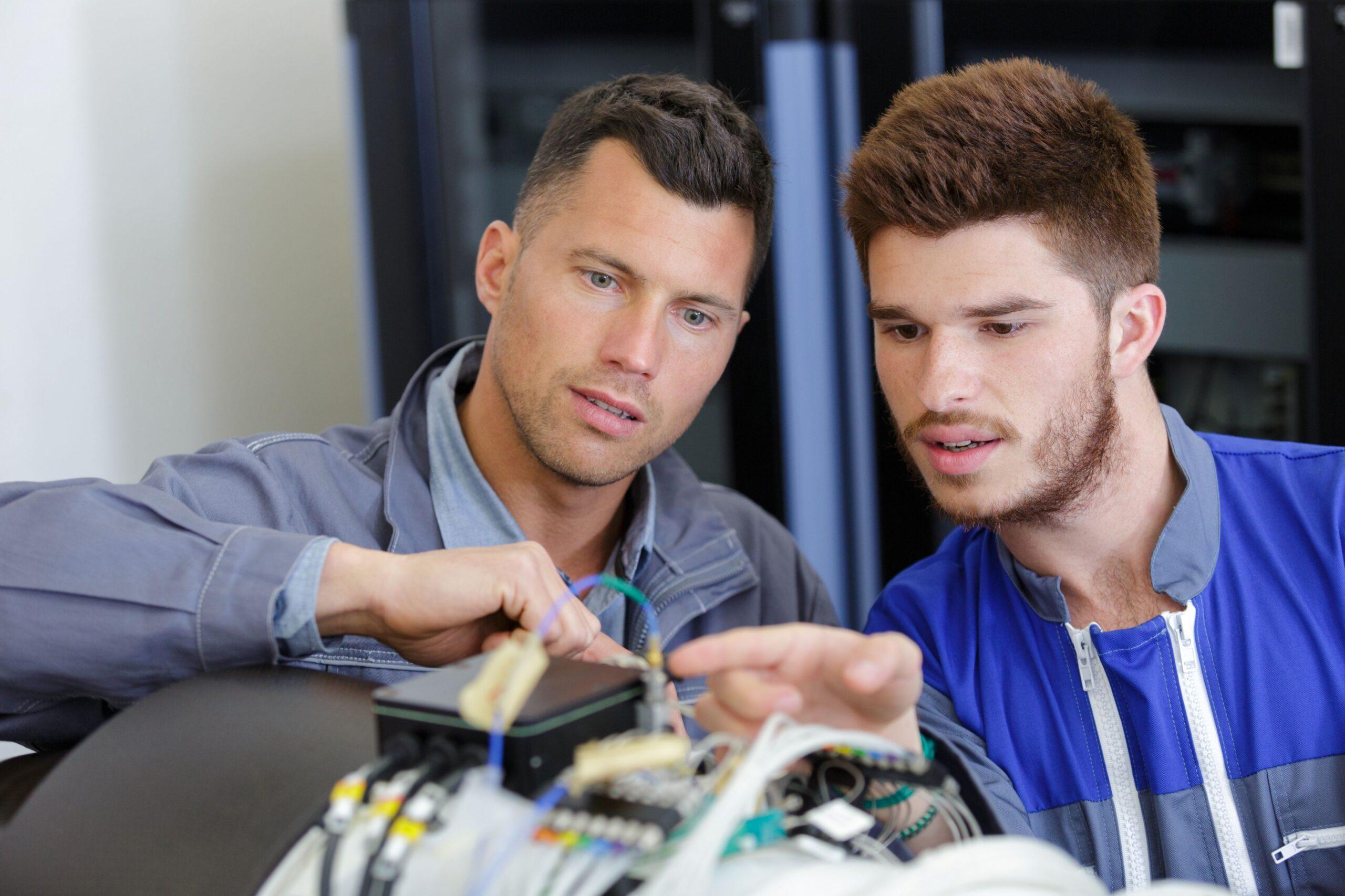 Zwei Techniker prüfen eine elektromechanische Baugruppe in der Baugruppemontage an einem modularen Industriearbeitsplatz